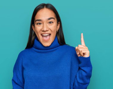 Sıradan bir kazak giyen Asyalı genç bir kadın başarılı bir fikri işaret ediyor. Heyecanlı ve mutlu. Bir numara.. 