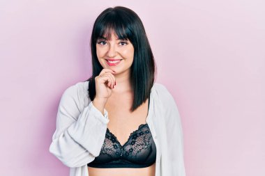 İç çamaşırı giyen genç İspanyol kadın kameraya kendinden emin bakıyor kollarını kavuşturup gülümseyerek ve çenesini kaldırarak. Olumlu düşünmek. 