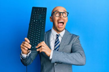 Bald man with beard holding keyboard angry and mad screaming frustrated and furious, shouting with anger looking up. 
