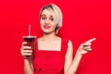 Genç, güzel sarışın kadın bir bardak kola içiyor gülümsüyor mutlu bir şekilde elini ve parmağını yana uzatıyordu. 