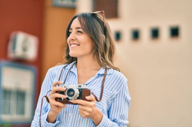 Genç İspanyol turist kadın şehirde klasik kamera kullanarak mutlu bir şekilde gülümsüyor..