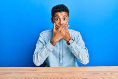 Genç, yakışıklı, Afro-Amerikan bir adam, gündelik giysiler içinde masada oturuyor ve ağzı yanlışlıkla ellerle kapatıyor. gizli kavram. 