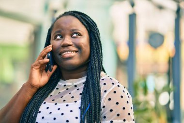 Genç Afrikalı Amerikalı kadın gülümsüyor. Şehirdeki akıllı telefondan mutlu bir şekilde konuşuyor..