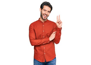 Gündelik kıyafetler giyen, gülümseyen ve kameraya göz kırpan genç İspanyol adam zafer işareti yapıyor. İki numara.. 