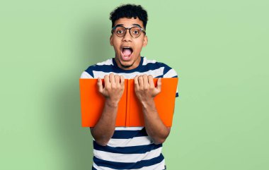 Genç Afro-Amerikalı bir adam gözlükleriyle kitap okuyor. Çılgınlığı kutluyor ve başarıya hayret ediyor. Gözleri açık, heyecanlı çığlıklar atıyor.. 