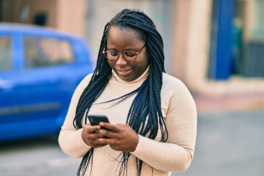 Genç Afrikalı Amerikalı kadın şehirde akıllı telefon kullanıyor..
