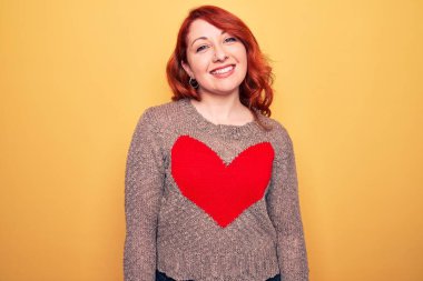 Genç, güzel, kızıl saçlı bir kadın. Sarı arka planda kalbi olan sıradan bir kazak giyiyor. Yüzünde mutlu ve havalı bir gülümseme var. Şanslı kişi..