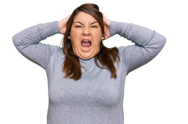 Güzel esmer ve cüsseli bir kadın gündelik kıyafetler giyiyor çılgın ve elleri başının üstünde korkmuş, ağzı açık şoktan korkmuş ve şaşırmış. 