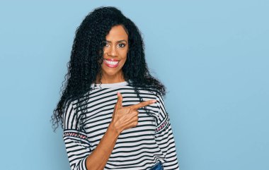 Orta yaşlı Afro-Amerikalı kadın, günlük kıyafetler giyiyor, neşeli, yüzünde mutlu ve doğal bir ifadeyle, elleri ve parmaklarıyla yüzünü gösteren bir gülümseme var. 