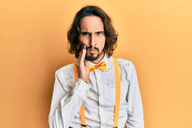Hippi gibi şık giyinen genç İspanyol bir adam diş ağrısı ya da diş hastalığından dolayı acı dolu bir ifadeyle dudaklarına dokunuyor. dişçi 