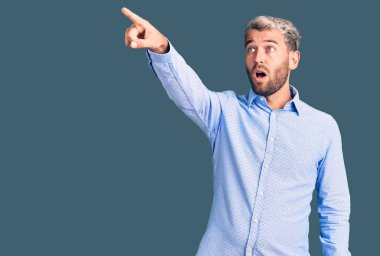 Zarif tişört giyen yakışıklı genç adam parmağını göstererek şaşırmış, ağzı açık, şaşırmış, ön tarafta bir şey var. 