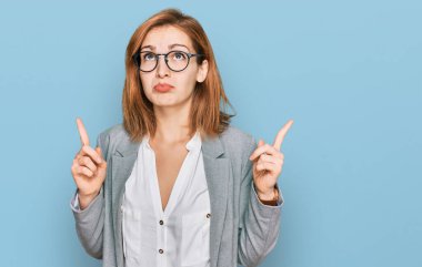 İş stili ve gözlük takan genç beyaz kadın üzgün ve üzgün görünüyor, parmaklarıyla yönü gösteriyor, mutsuz ve depresif.. 