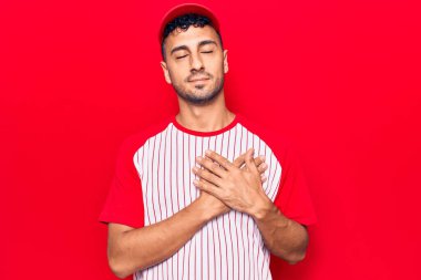 Beyzbol üniforması giyen, elleri göğsünde gülümseyen, gözleri kapalı, yüzünde minnet ifadesi olan genç İspanyol bir adam. sağlık kavramı. 