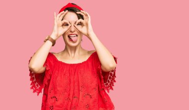 Kısa saçlı, günlük yaz kıyafetleri giyen ve diyabet yapan genç esmer kadın dürbün gibi jest yapıyor, gözleri parmaklarından bakıyor. çılgın ifade. 