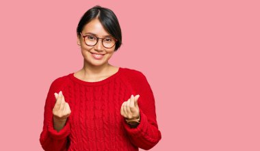 Kısa saçlı, günlük süveter giyen ve gözlük takan genç ve güzel İspanyol bir kadın. Elleriyle para hareketi yapıyor. Maaş ödemesi istiyor. 