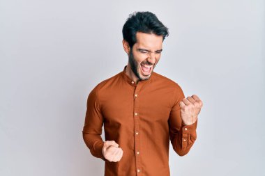 Gündelik giysiler giyen genç İspanyol adam şaşkınlık ve şaşkınlık içinde kollarını kaldırarak ve gözlerini kapayarak başarıyı kutluyor. 