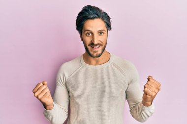 Gündelik kazak giyen genç İspanyol adam kollarını kaldırıp, gözlerini açarak başarıyı kutluyor ve şaşırıyor. Kazanan konsept. 