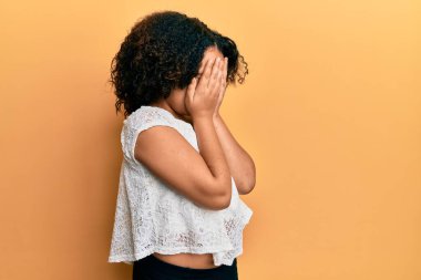 Afro saçlı, sıradan kıyafetler giyen, suratını ellerle örten ve ağlayan genç bir kız. depresyon kavramı. 