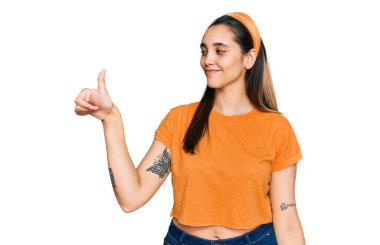 Genç İspanyol kadın günlük kıyafetler giyiyor. Gururlu görünüyor, gülümsüyor. Kenarda baş parmak hareketi yapıyor. 