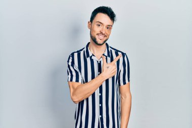 Yüzünde mutlu ve doğal bir ifade olan, elleri ve parmaklarıyla işaret eden, güler yüzlü, gündelik kıyafetler giyen genç İspanyol adam. 