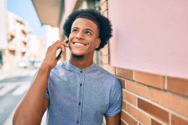 Genç Afrikalı Amerikalı gülümseyen mutlu bir adam şehirdeki akıllı telefondan konuşuyor..