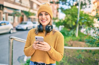 Şehirde akıllı telefon ve kulaklık kullanan genç sarışın kadın..