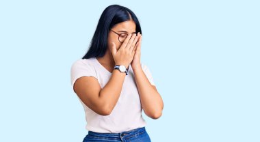 Genç, güzel Asyalı bir kız, günlük kıyafetler ve ağlarken suratını ellerle örten üzgün bir gözlük takıyor. depresyon kavramı. 