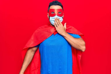 Süper kahraman kostümü giyen genç İspanyol bir adam ve ağızlarını ağızla kapatan tıbbi bir maske, şok geçirmiş ve hata yapmaktan korkan. şaşırmış ifade 