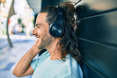 Genç İspanyol gülümseyen adam şehirde kulaklık takarak müzik dinlemekten mutlu oluyor..