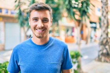 Genç beyaz adam gülümseyerek şehirde mutlu mesut yürüyor..