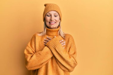 Middle age caucasian woman wearing wool winter sweater and hat smiling with hands on chest with closed eyes and grateful gesture on face. health concept. 