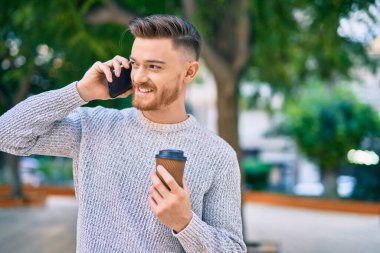 Kafkasyalı genç adam akıllı telefondan konuşuyor parkta kahve içiyor..