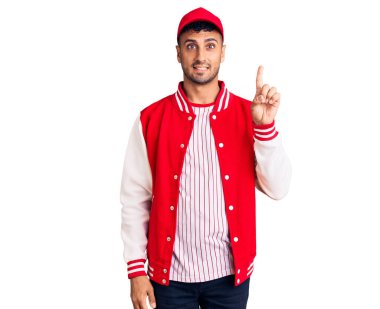 Beyzbol üniforması giyen genç İspanyol bir numarayı gösterip işaret ederken kendinden emin ve mutlu gülümsüyor.. 