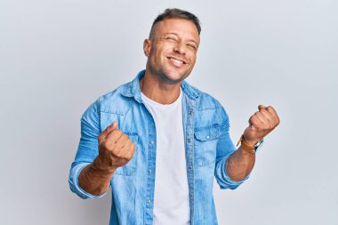 Sıradan bir kot ceket giyen yakışıklı kaslı adam. Başarının heyecanı içinde kolları havada ve gözleri kapalı zaferi kutlarken gülümsüyor. Kazanan konsept. 