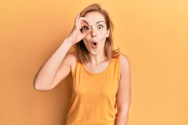 Kolsuz tişörtlü, sıradan giyinen genç beyaz kadın şaşırmış yüz ifadesiyle şaşırmış, parmaklarından içeri bakıyor. İnançsız ifade. 