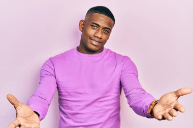 Genç siyah adam, günlük pembe süveter giyiyor, gülümsüyor, yardım eli uzatıyor ve kabul ediyor.. 