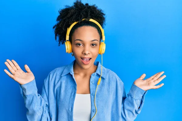 年轻的非洲裔美国女孩 一边用耳机听音乐 一边笑着庆祝胜利 一边高举双手庆祝胜利 — 图库照片