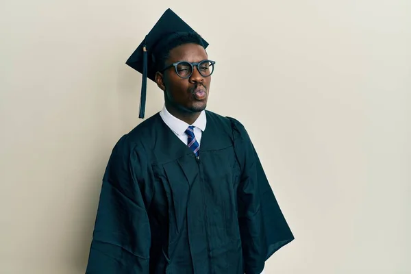 Przystojny Czarny Mężczyzna Ubrany Czapkę Dyplomem Szlafrok Patrzący Kamerę Dmuchający — Zdjęcie stockowe