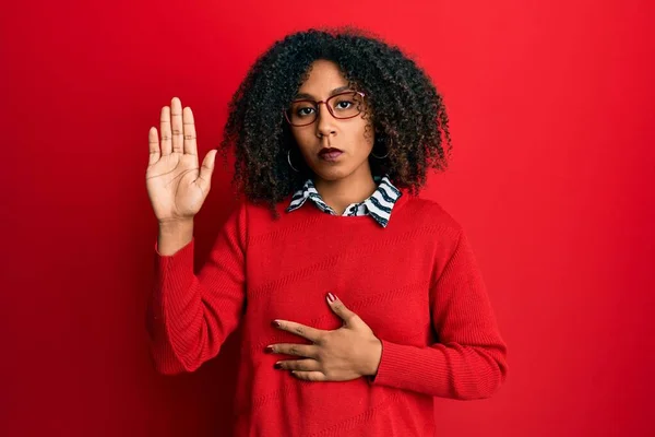 Beautiful african american woman with afro hair wearing sweater and glasses swearing with hand on chest and open palm, making a loyalty promise oath