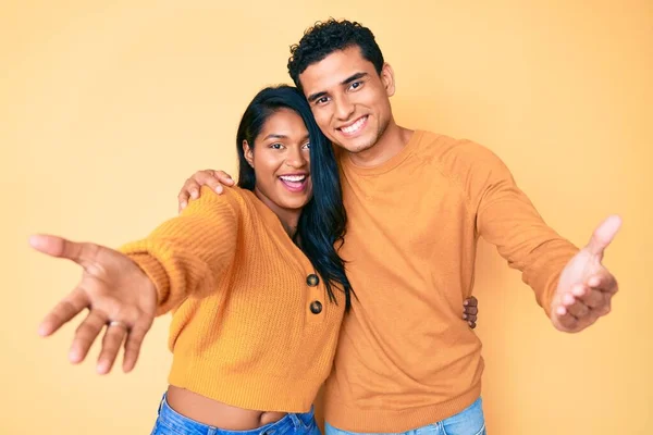 美しいラテン語の若いカップル一緒にカジュアルな服を着て一緒に抱擁のために開いて腕を笑みを浮かべてカメラを見て 幸せを受け入れる陽気な表情 — ストック写真