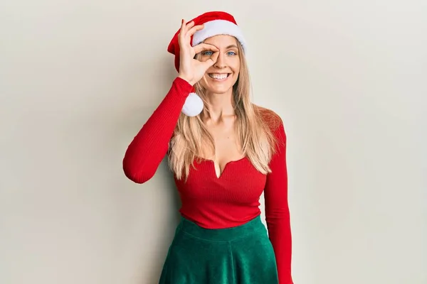 美しい白人女性を身に着けていますクリスマスの衣装と帽子を身に着けています手笑顔でOkジェスチャー 幸せな顔で指を通して見る目 — ストック写真