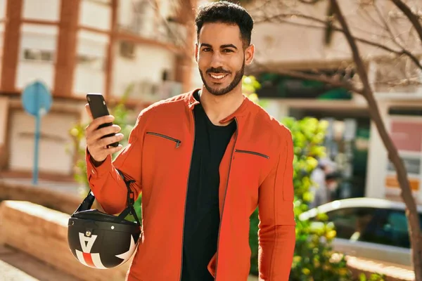 Genç İspanyol adam şehirde moto miğferi tutan akıllı telefon kullanıyor..