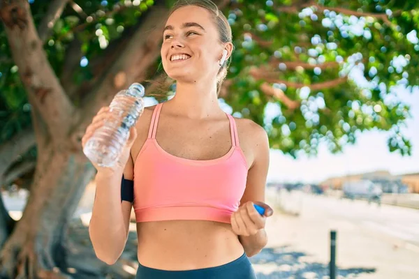 Genç sarışın sporcu şehirde bir şişe su içerek egzersiz yapıyor.