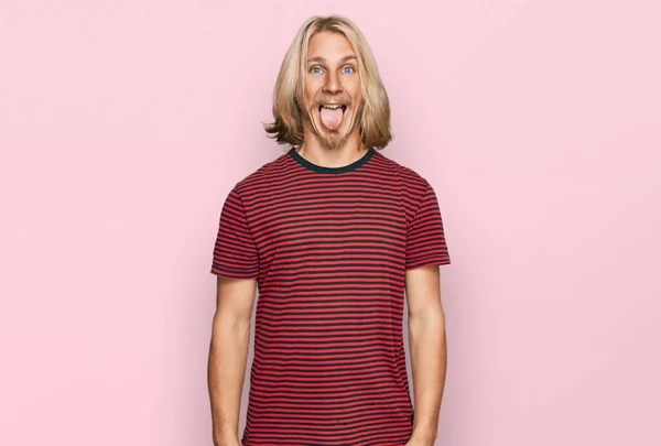 金髪の長髪の白人男性が面白い表情で幸せ舌を突き出すカジュアルな縞模様のTシャツを着ています 感情の概念 — ストック写真