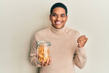 Genç, yakışıklı İspanyol adam elinde makarna kavanozuyla gururla bağırıyor zaferi ve başarıyı kutluyor. 