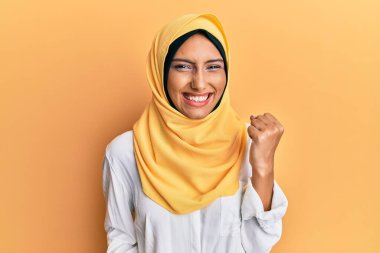 Young brunette arab woman wearing traditional islamic hijab scarf celebrating surprised and amazed for success with arms raised and eyes closed. winner concept. 