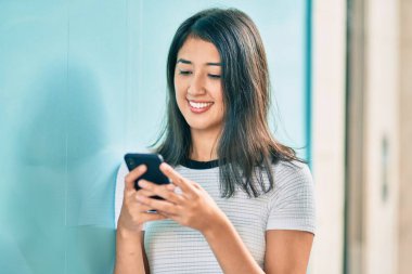 Genç İspanyol kadın şehirde akıllı telefon kullanarak mutlu bir şekilde gülümsüyor..