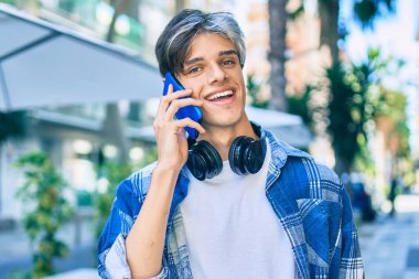 Genç İspanyol adam gülümsüyor. Akıllı telefonla konuşuyor ve şehirde kulaklık takıyor..