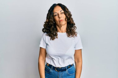 Orta yaşlı İspanyol kadın, günlük beyaz tişört giyiyor. Yüzünde ciddi bir ifade var. Basit ve doğal bir şekilde kameraya bakıyorsun.. 