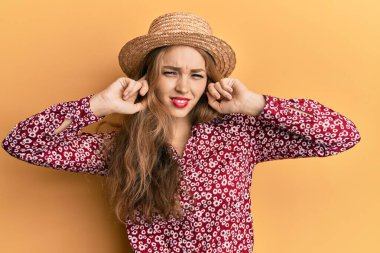 Güzel sarışın beyaz kadın, yüksek sesli müzik sesi için kulaklarını parmaklarıyla kapatan yaz şapkası takıyor. sağır kavramı. 